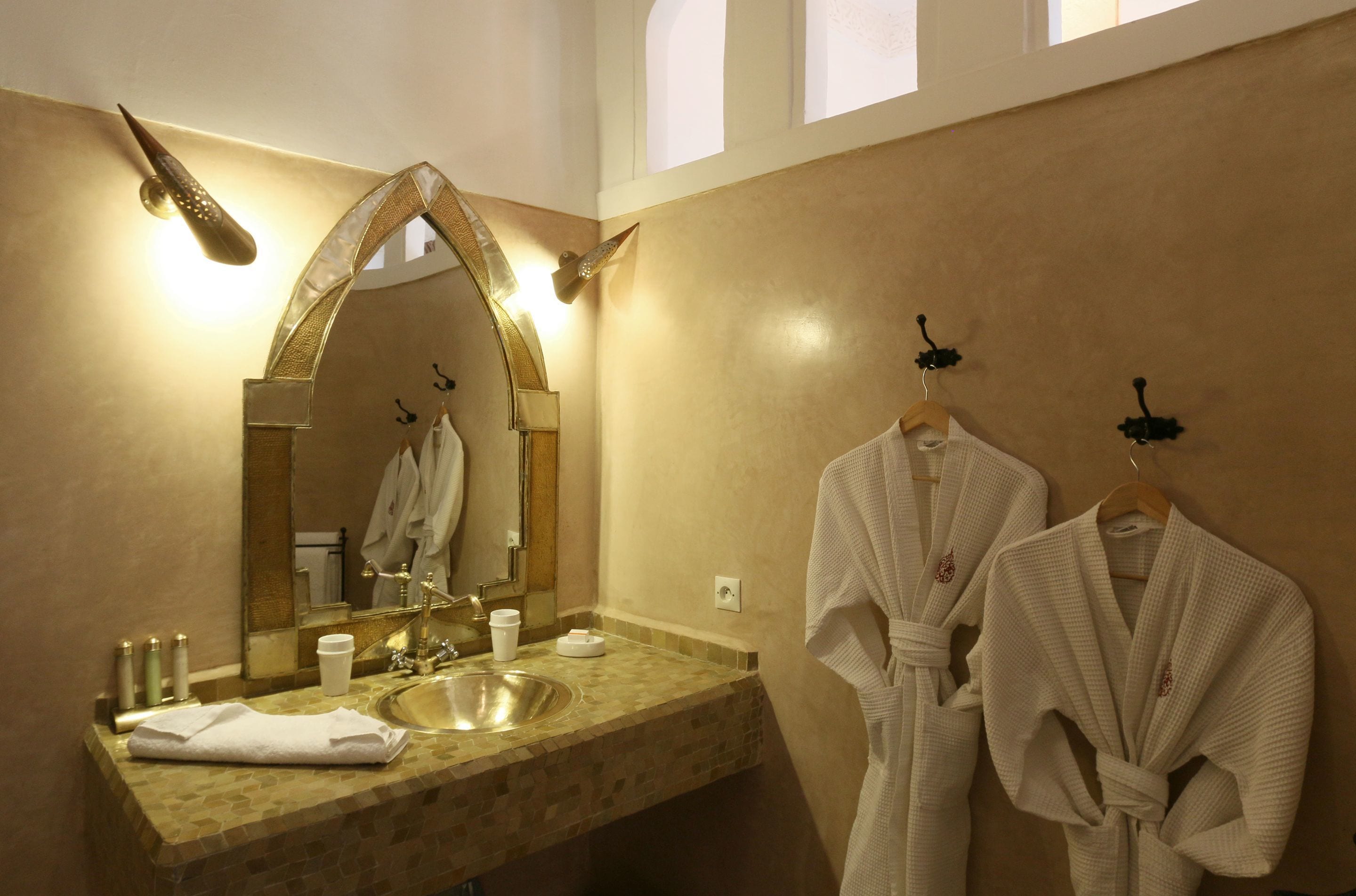 Une salle de bain avec un grand miroir, un lavabo et deux peignoirs suspendus à des crochets.