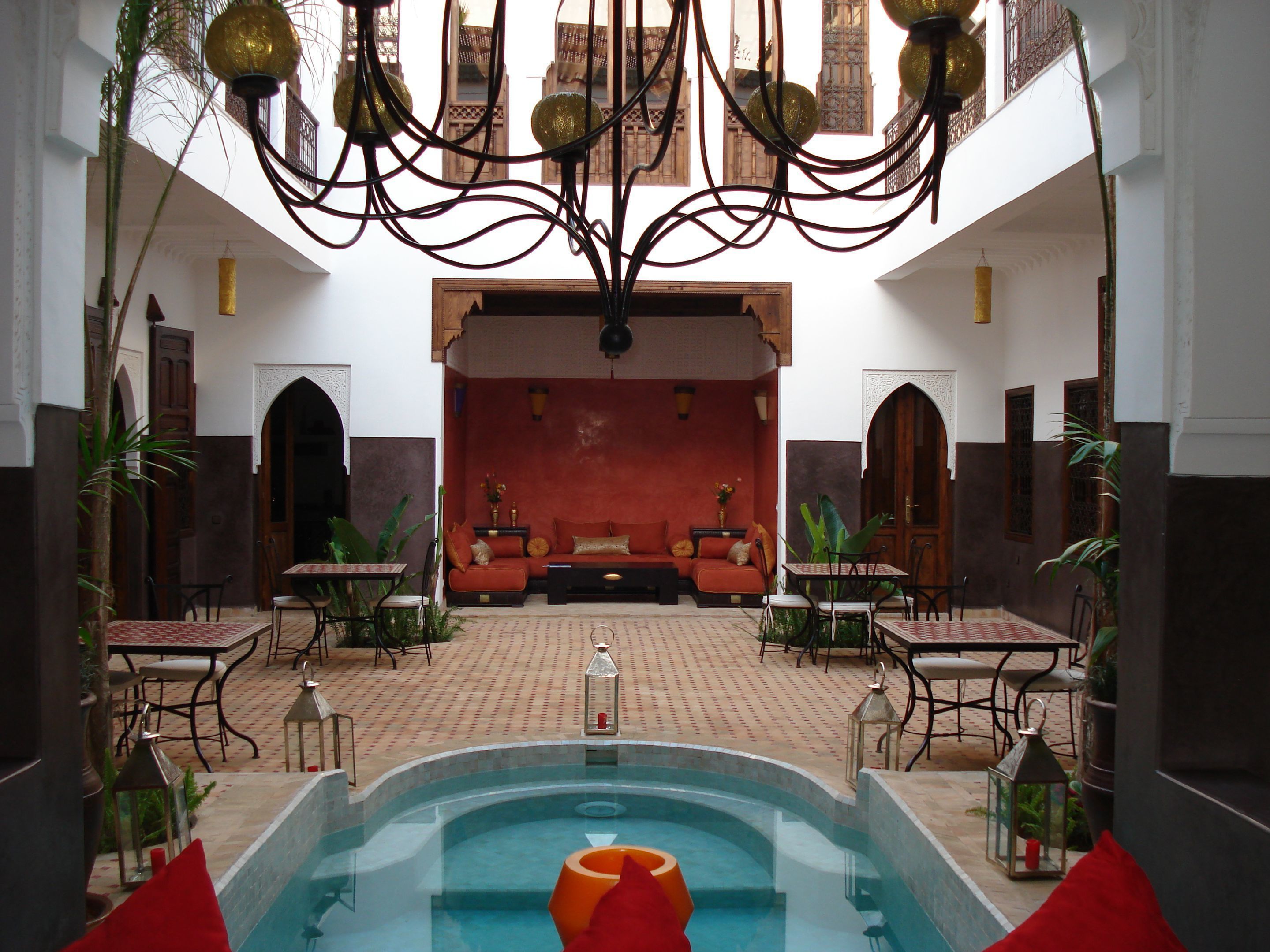 A pool area with seating and tables, surrounded by walls with decorative arches and a ceiling with hanging lights.