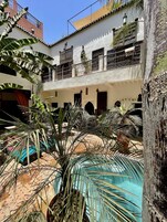 A courtyard with a pool, palm trees, and a building with balconies and arched doorways.