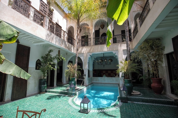 A courtyard with a central pool, surrounded by potted plants and a tiled floor.