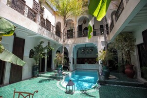 Un cortile con piscina centrale, circondato da piante in vaso e un pavimento piastrellato.