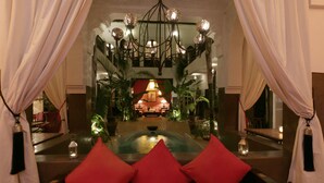 A luxurious lobby with a central seating area, a chandelier, and potted plants.