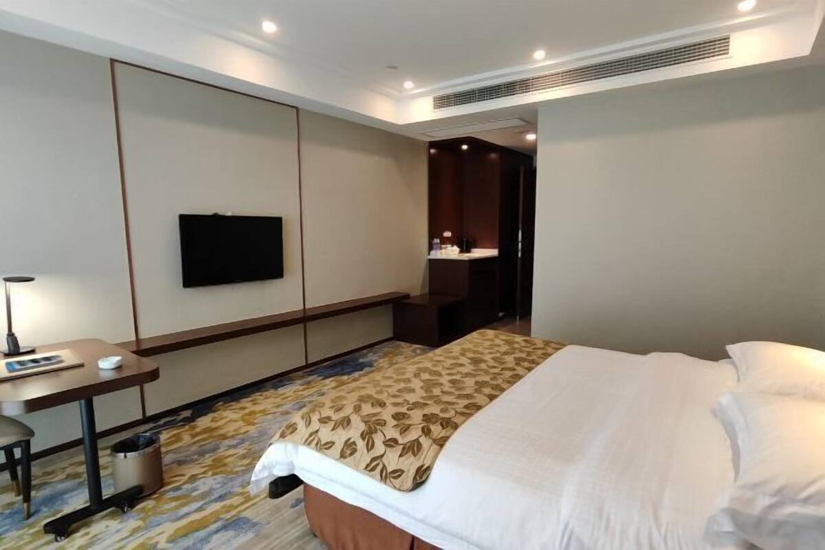 A hotel room with a bed, a desk, a chair, a television, and a bathroom visible through an open door.