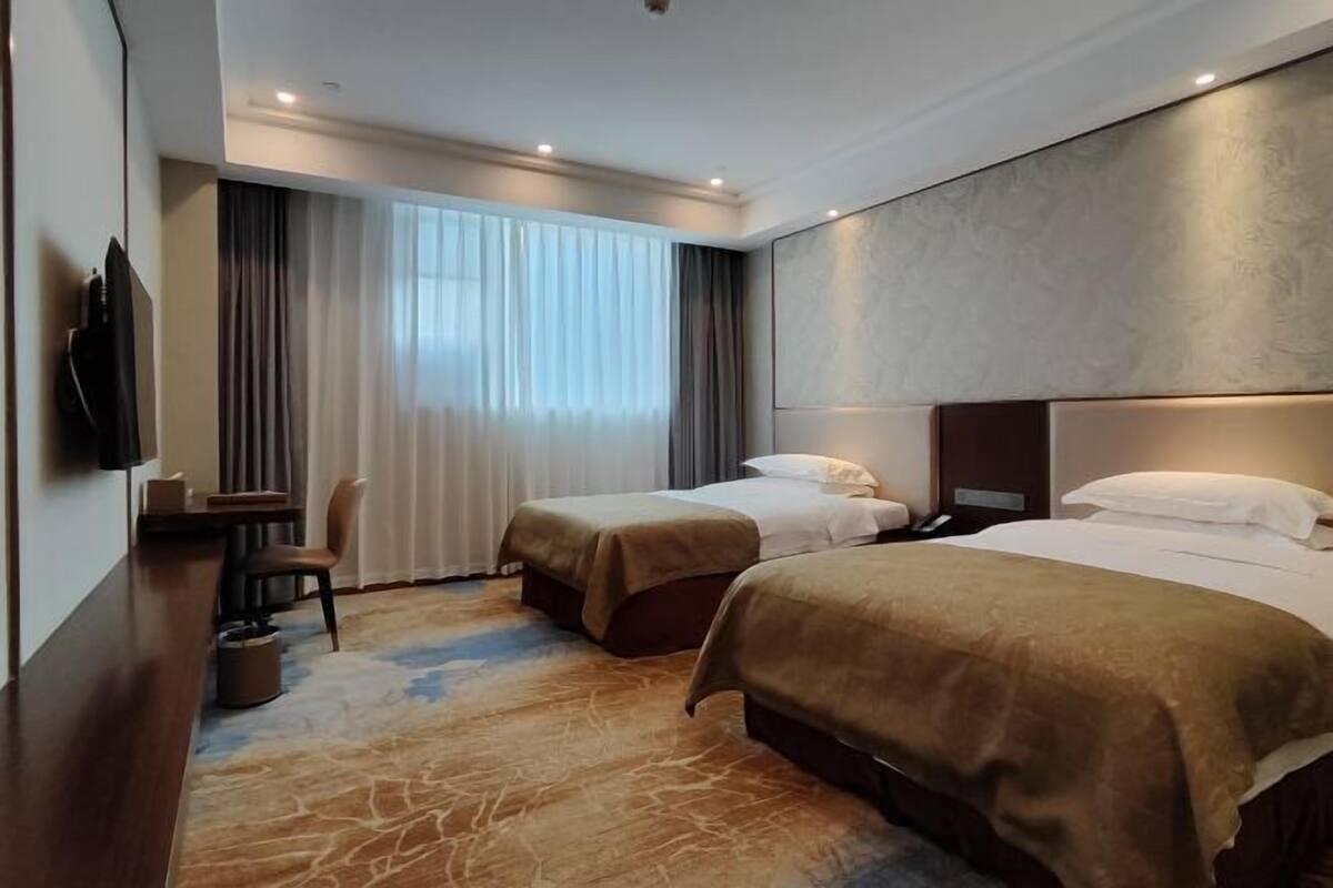 A hotel room with two beds, a desk, a chair, and a TV.