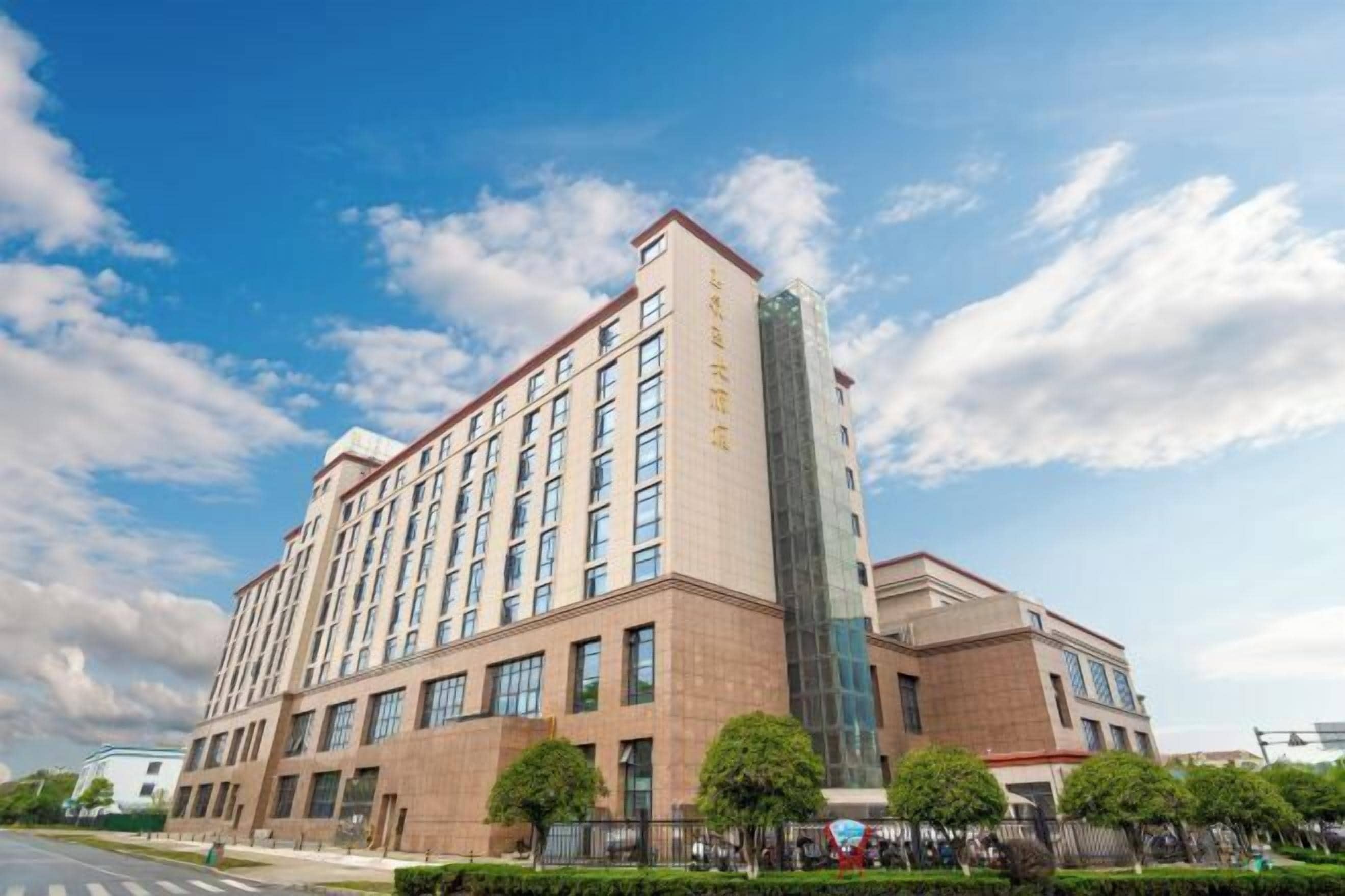 Ein mehrstöckiges Hotel mit einem markanten Glasturm, einer Ziegel-Fassade und blauem Himmel.