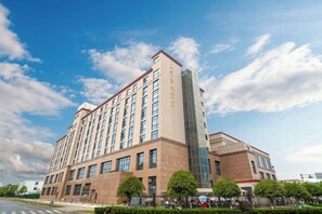 Um hotel com vários andares, uma torre de vidro destacada e fachada de tijolos, sob um céu claro.