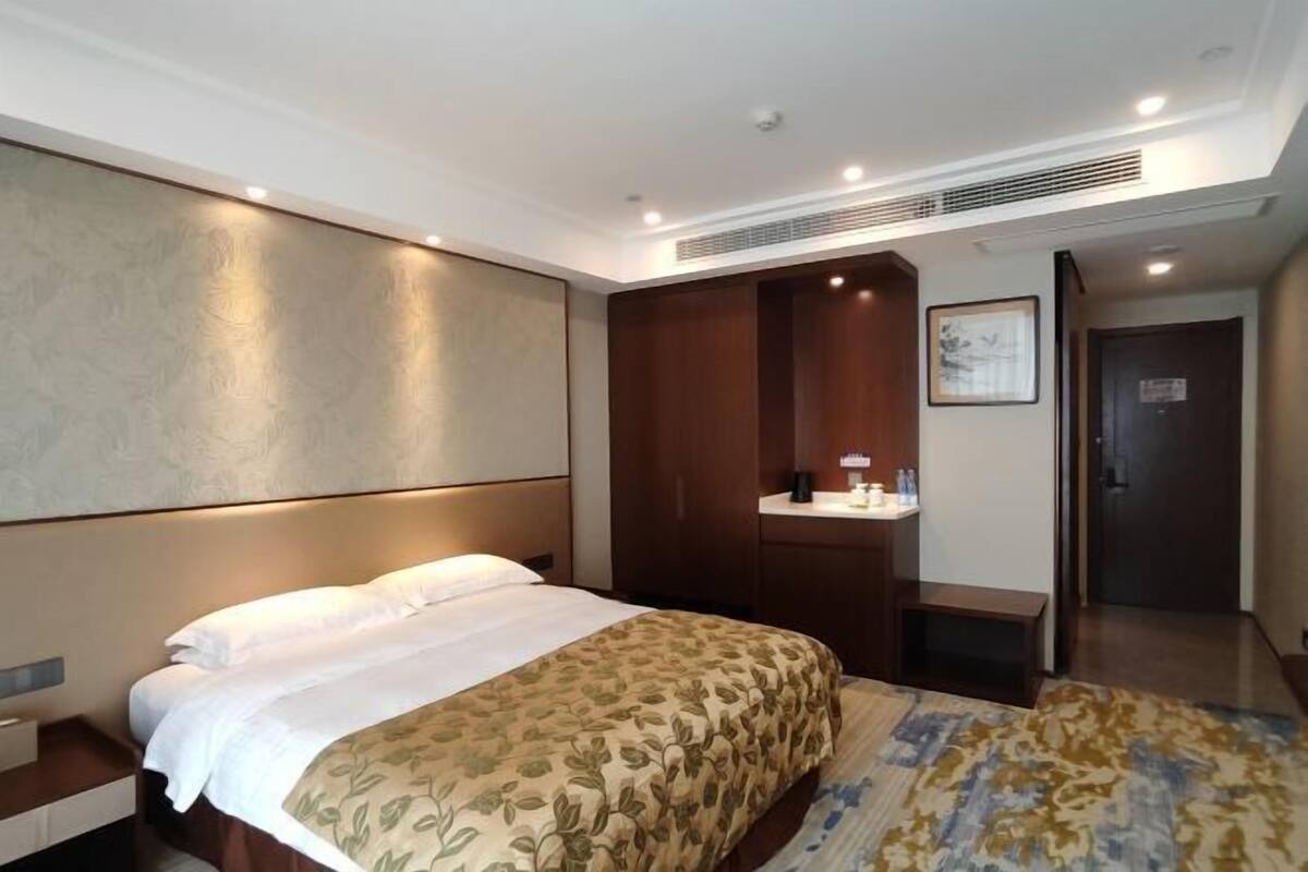 A hotel room with a bed, a nightstand, a desk with a chair, a mirror, and a door.