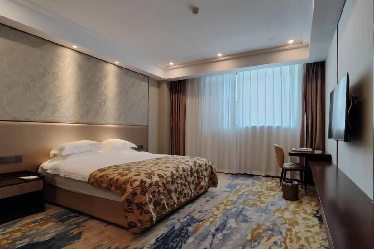 A hotel room with a large bed, a desk, a chair, and a TV on the wall.