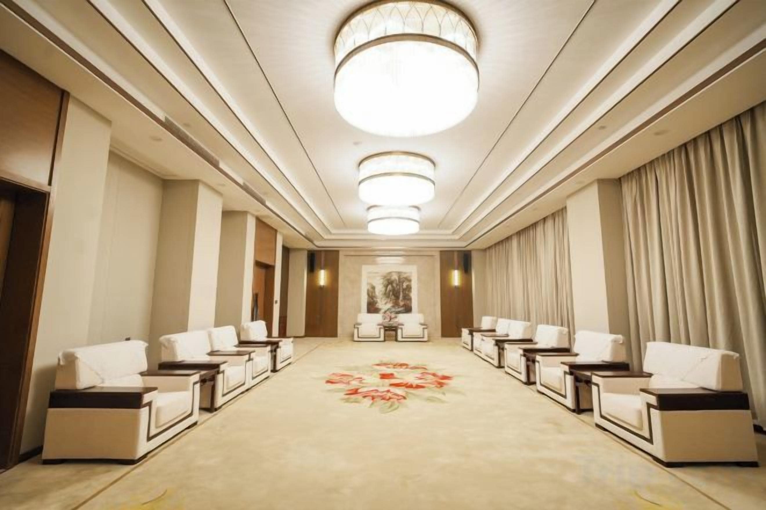 A hotel corridor with a carpeted floor, seating area with chairs, and a large chandelier.