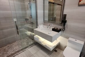 Uma casa de banho moderna com chuveiro de vidro, lavatório branco com espelho em cima e sanita.