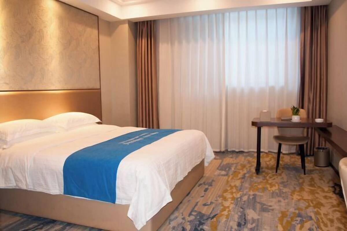 A hotel room with a bed, a desk, a chair, and a window with curtains.