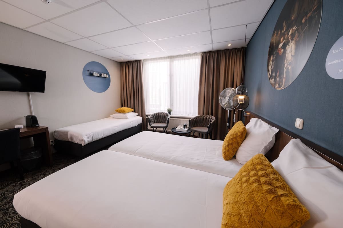 A hotel room with two beds, a desk, a chair, a TV, and a large window with curtains.