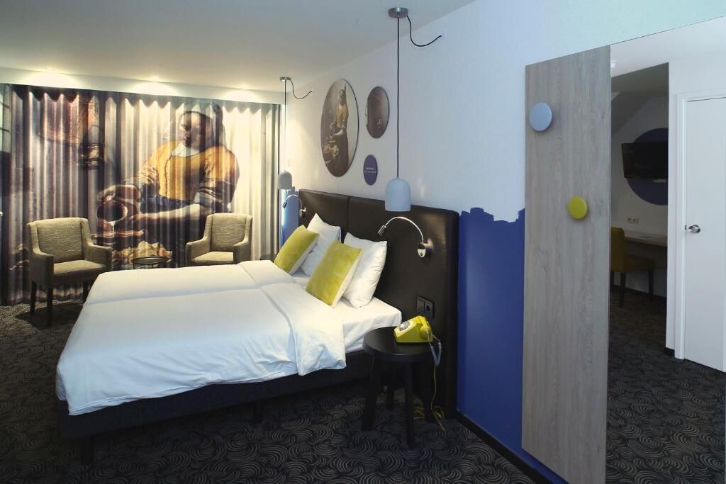 Een hotelkamer met een groot bed, twee stoelen, een bureau en een spiegel.