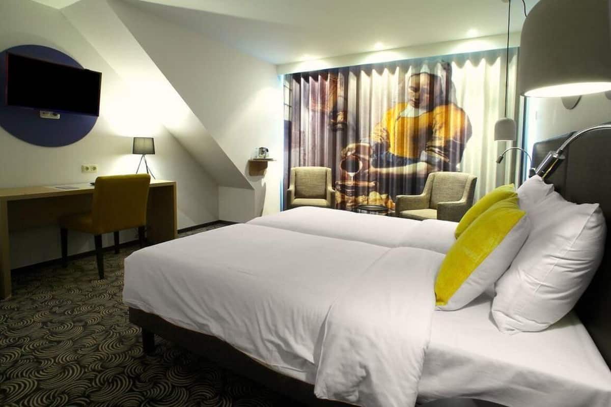 A hotel room with a bed, a desk, a chair, and a television mounted on the wall.