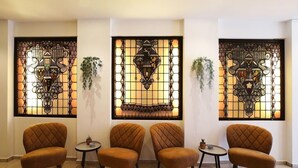 A lobby with four brown armchairs, a small table, and decorative stained glass panels. - Hotel de Koophandel (Delft)