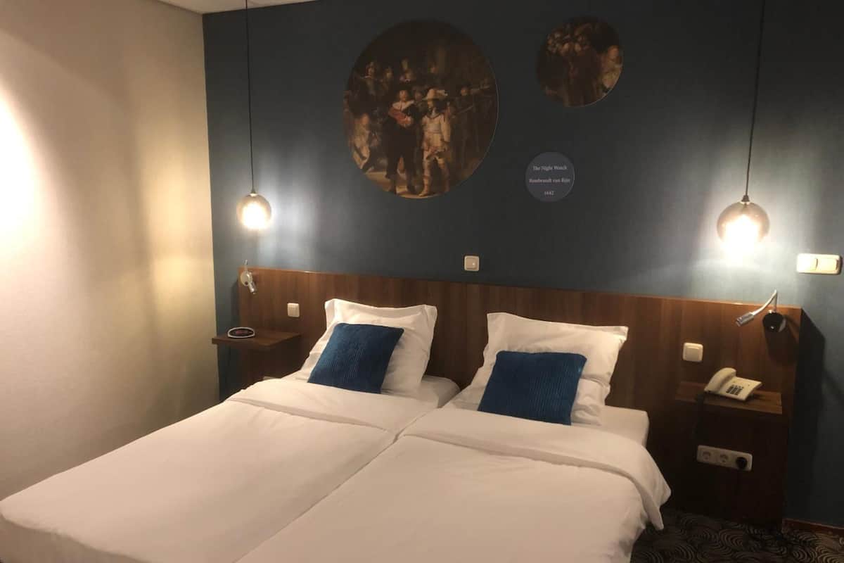 A double bed with white and blue bedding, two bedside tables with lamps, and a wall with three circular artwork pieces.