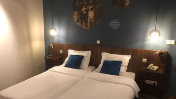 Ein Doppelbett mit weißer und blauer Bettwäsche, zwei Nachttische mit Lampen und eine Wand mit drei runden Kunstwerken.