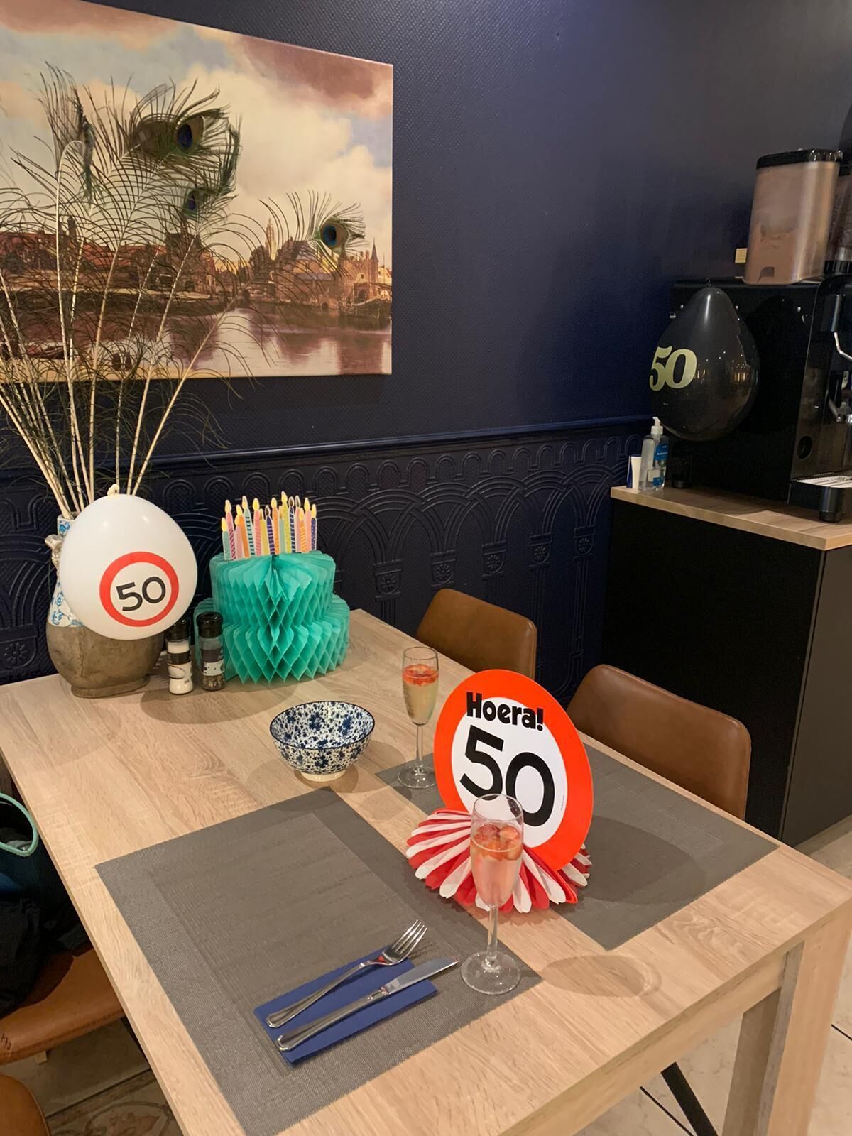 A dining table set with a glass of champagne, a bowl, cutlery, and a 'Hoera! 50' sign.