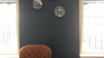 Een kamer met een donkere muur, een bruine stoel, een klein rond tafeltje met een witte dienblad, en vier decoratieve borden aan de muur.