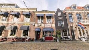 A hotel with a red entrance door, outdoor seating, and a sign reading "Hotel." - Hotel de Koophandel (Delft)