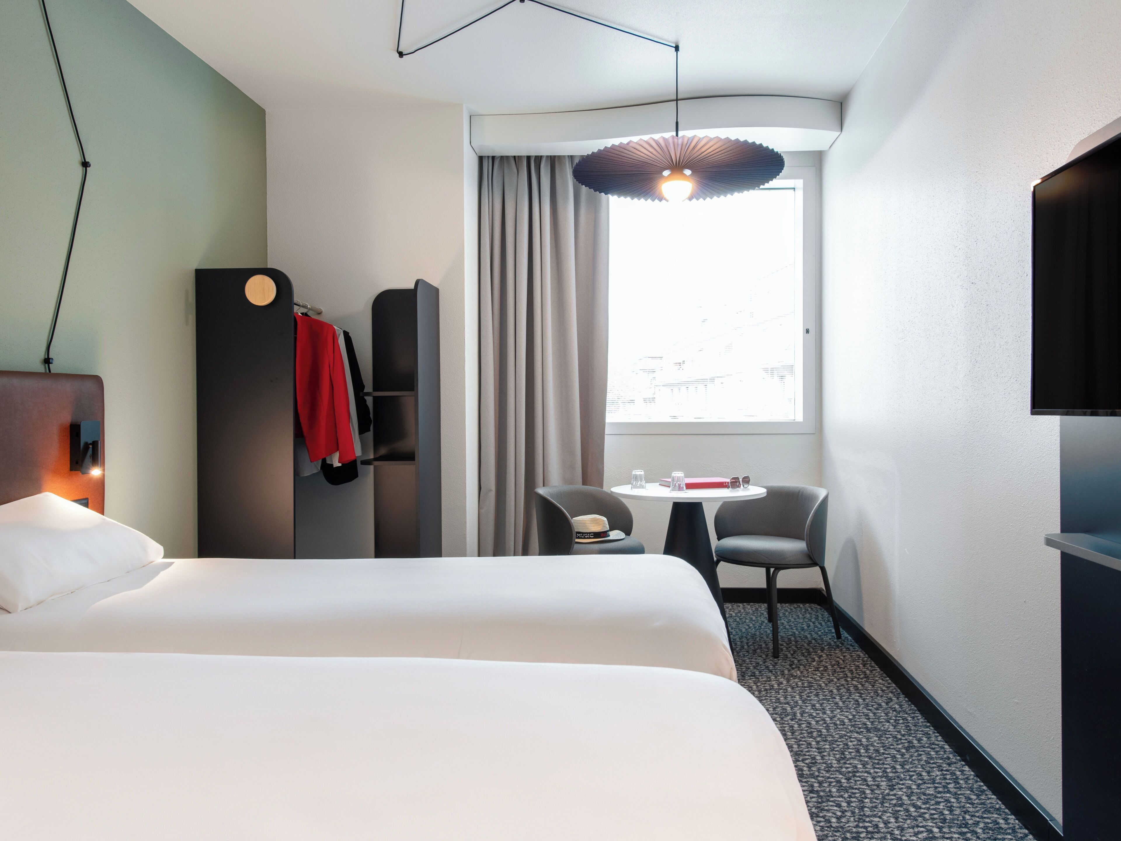 A hotel room with a bed, a desk with a chair, a television, and a window with curtains.