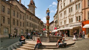 Une place publique agrémentée d’une fontaine, d’escaliers et entourée de bâtiments historiques.