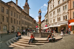 A public square with a fountain, steps, and surrounding historic buildings.