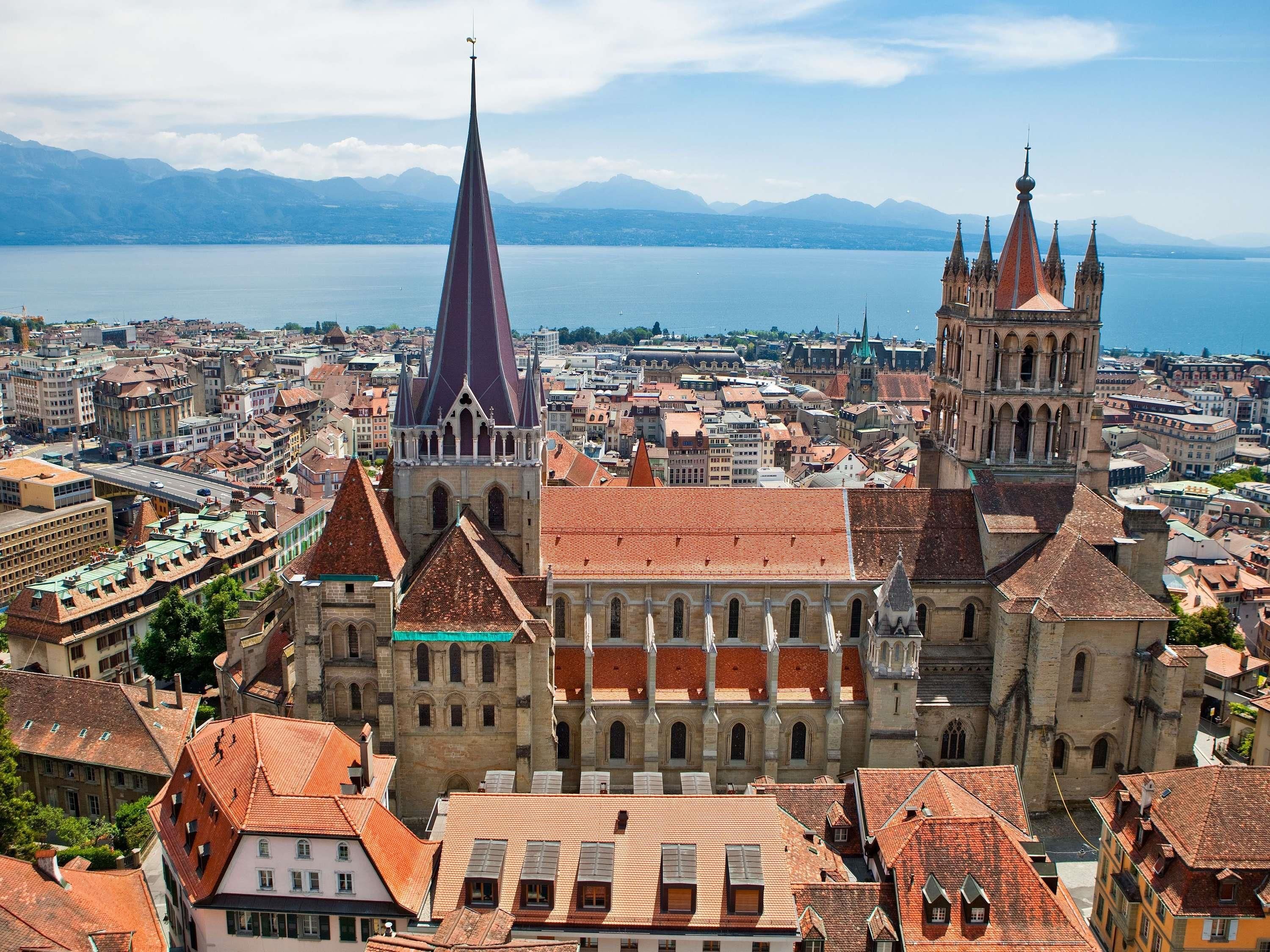 A cityscape with historic buildings, a prominent church spire, and a body of water in the background.