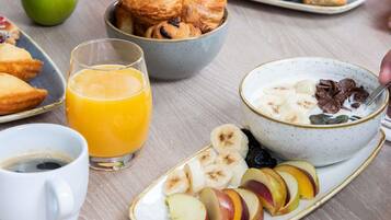 A breakfast setting with croissants, a bowl of cereal with fruit, a glass of orange juice, and a plate of sliced apples.