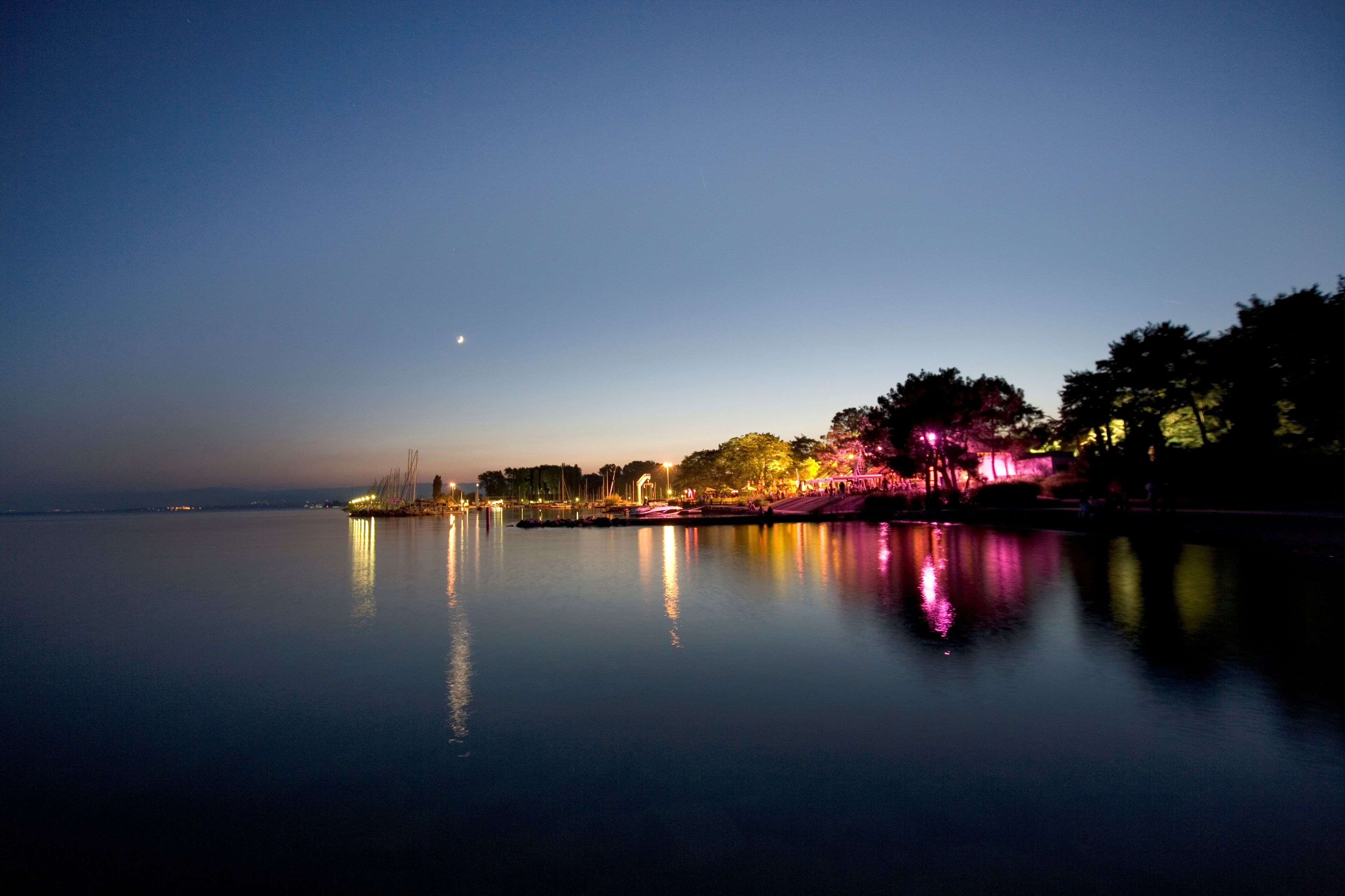 A calm body of water reflecting lights from a distant shoreline.