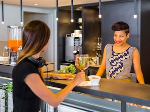 Zona de bar moderna con una máquina de café, un vaso de bebida y una persona sosteniendo un vaso.