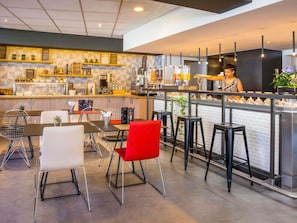 A modern cafe interior with a bar area, seating arrangements, and a counter with a barista. - ibis Lausanne Centre (Lausanne)