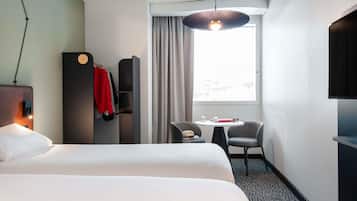 A hotel room with a bed, a desk with two chairs, a TV, and a window with curtains.