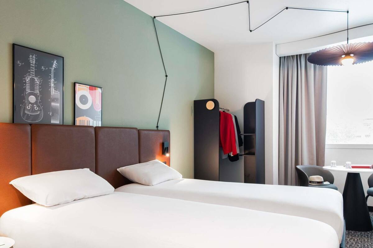 A hotel room with a bed, a desk, a chair, a coat rack, and a window with curtains.