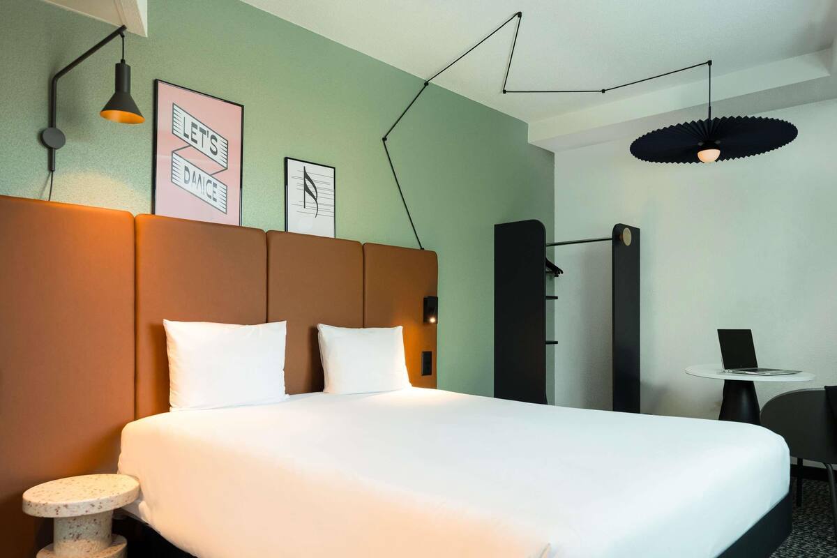 Een hotelkamer met een bed, een bureau, een stoel, een krabpaal en een wandplank.