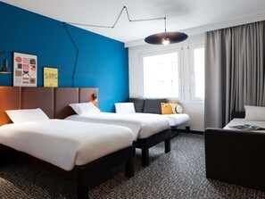 Une chambre d’hôtel avec deux lits, un canapé, un bureau et une grande fenêtre avec des rideaux.