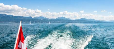 A boat with a flag, water, and mountains in the background.