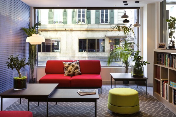 Una sala de estar moderna con un sofá rojo, un reposapiés amarillo, una mesa de centro y una estantería.