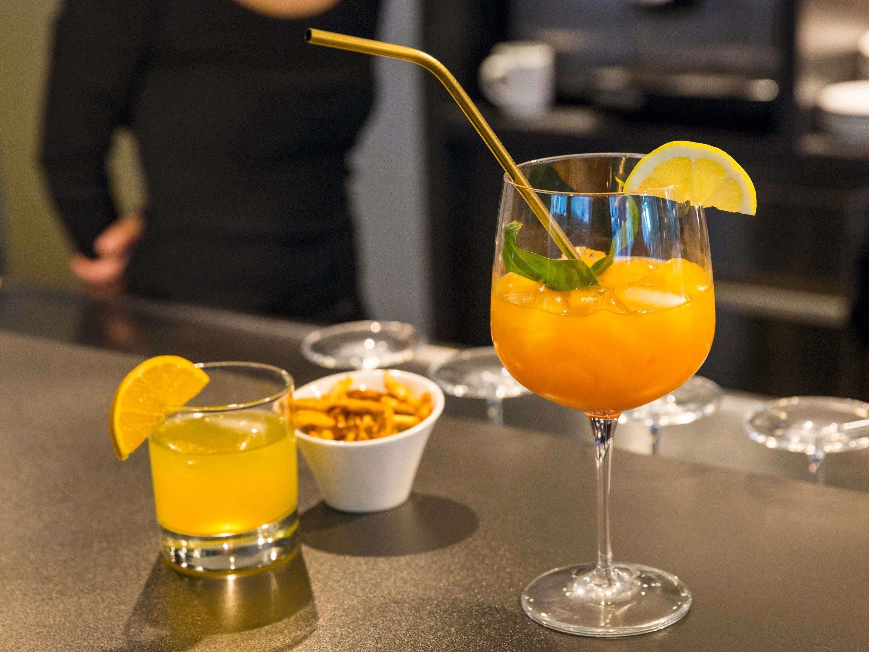 Un bar avec deux verres contenant des boissons de couleur orange, l’un décoré d’une tranche de citron et muni d’une paille, et un bol de frites en arrière-plan.