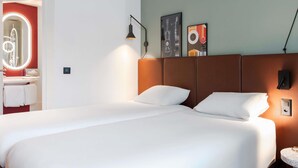 A hotel room with a large bed, a bathroom with a mirror, and a wall with two framed pictures.