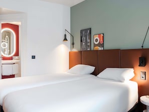 A hotel room with a large bed, a bathroom with a mirror, and a wall with two framed pictures.