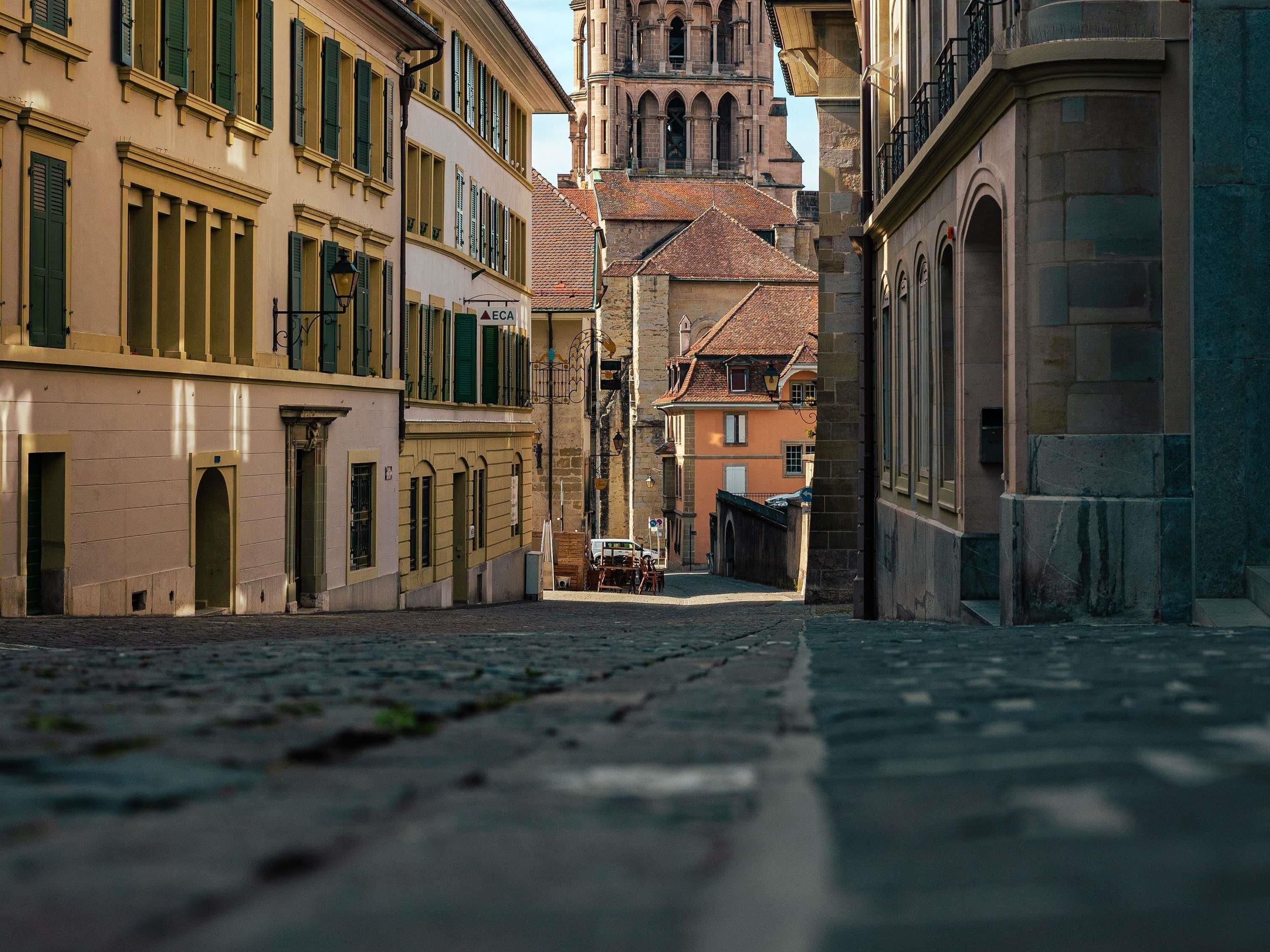 Une rue pavée bordée de bâtiments historiques, le clocher d’une église qui se profile au loin, et une ruelle étroite.