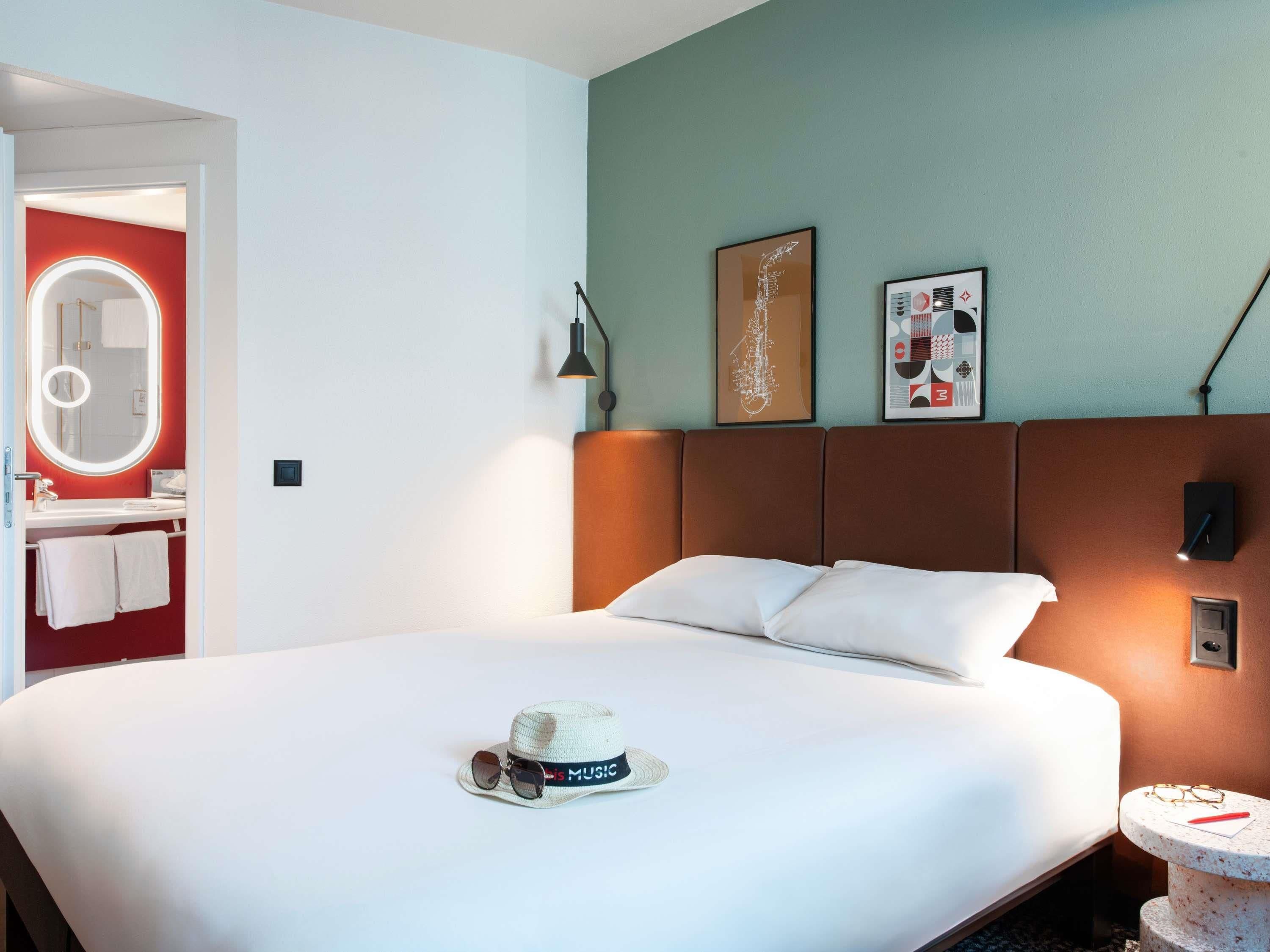 A hotel room with a bed, a round mirror with a light, a headboard, and two framed pictures on the wall.