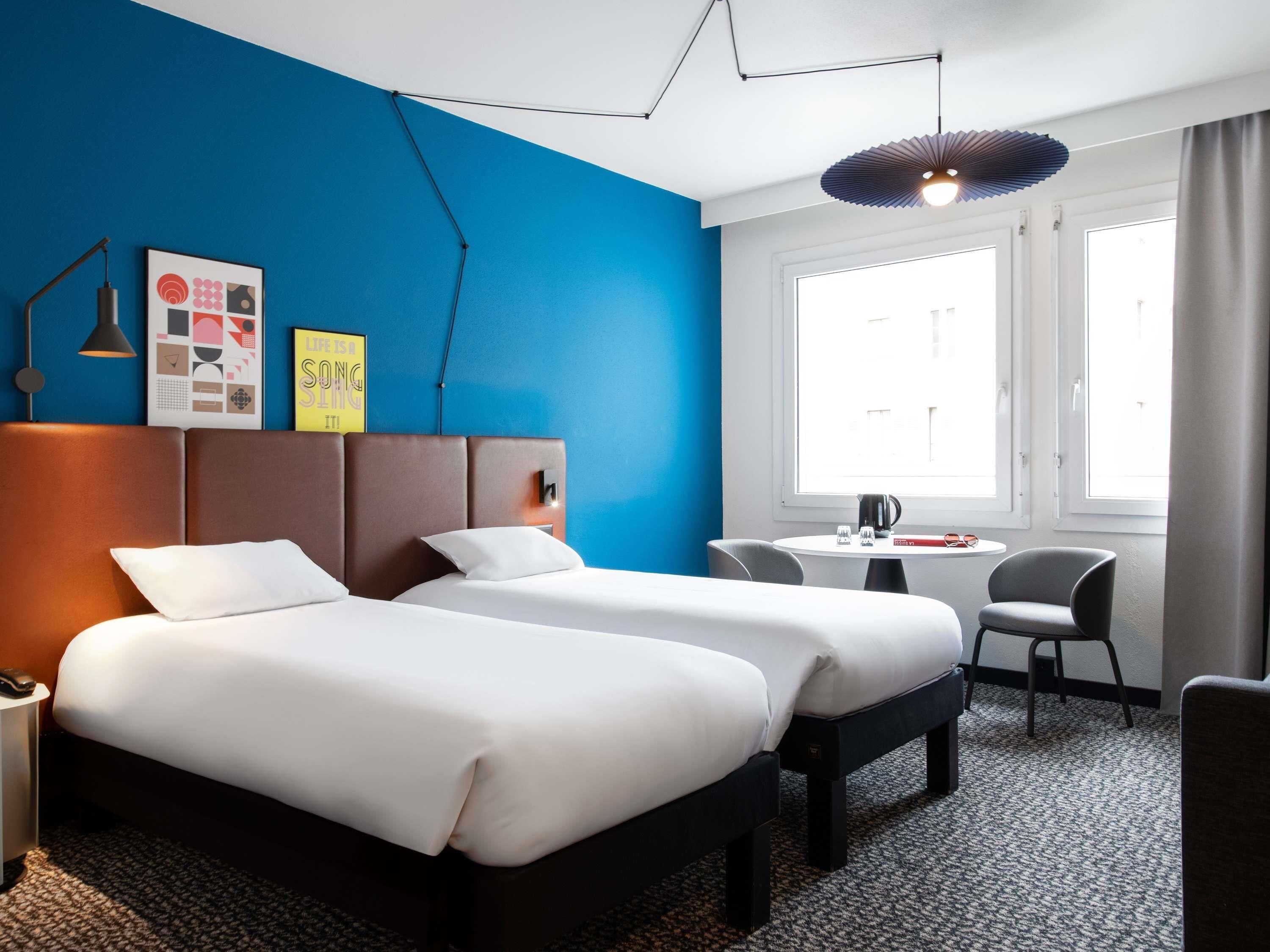 A hotel room with two beds, a desk, and a chair.