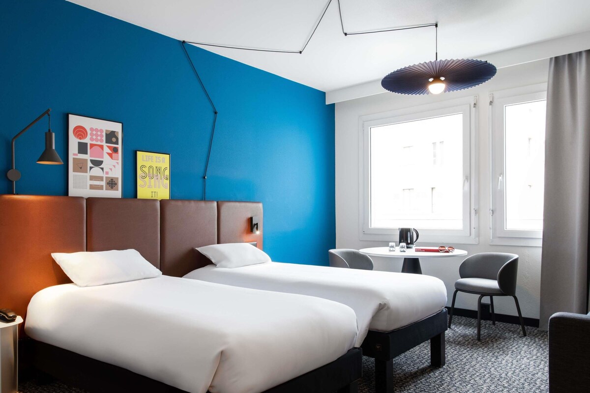 Et hotelværelse med to senge, et skrivebord og en stol.
