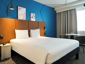 Habitación de hotel con una cama grande, una mesita de noche con un teléfono, una pequeña mesa con dos vasos y una silla.