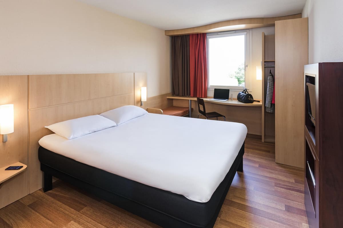 Une chambre d’hôtel avec un grand lit, un bureau avec un ordinateur portable, une chaise et une télévision.