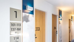 A hotel hallway with numbered doors, a directional sign, and a textured wall. - ibis Karlsruhe Hauptbahnhof (Karlsruhe)