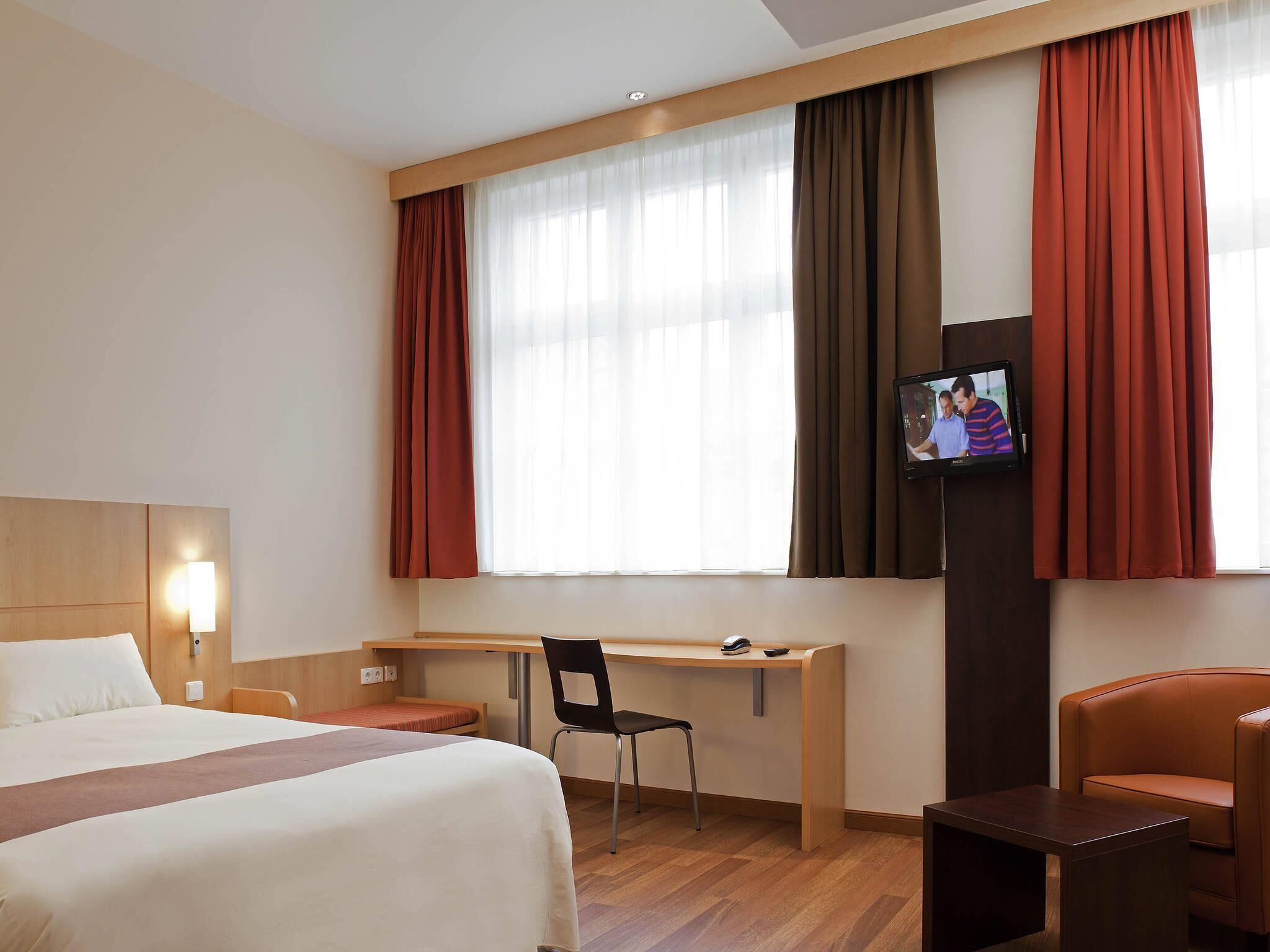 A hotel room with a bed, desk, chair, TV, and a sofa.