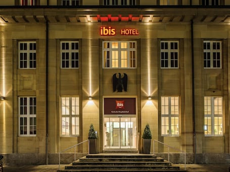 Ein Hauseingang eines Hotels mit einem gut sichtbaren 'ibis HOTEL'-Schild, einer Glastür und einer Treppe, die zum Eingang führt.. ibis Karlsruhe Hauptbahnhof